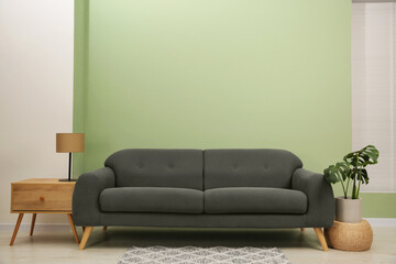 Wall Mural - Stylish sofa, side table and houseplant near green wall indoors