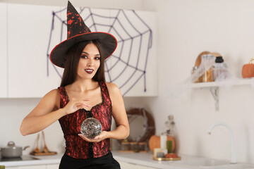 Poster - Beautiful young happy Asian woman dressed as witch for Halloween with crystal ball in decorated kitchen