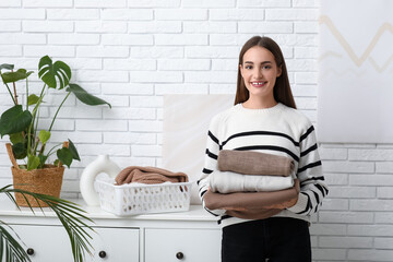 Poster - Young woman with stack of warm sweaters at home