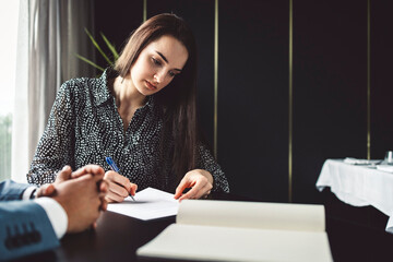 Two business people in business clothes are sitting in an office looking at a contract. One person is giving advice to the other. After signing the contract, they shake hands. Together they look out o