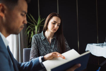 Two business people in business clothes are sitting in an office looking at a contract. One person is giving advice to the other. After signing the contract, they shake hands. Together they look out o