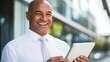 © BloomArt - A smiling businessman wearing a white shirt and tie holds a tablet in front of an office building.