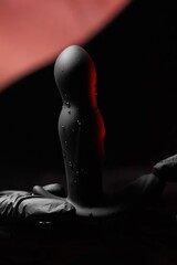 Wall Mural - Silicone anal vibrator in female hands in black latex gloves and a black dress on a red background. Massager with multiple speeds. Products for sex shops, adult gifts for couples.