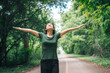 © NanSan - An Asian woman is standing happily in a green forest park, enjoying the fresh air and nature. She takes a deep breath, looks up at the morning sunlight, and feels relaxed and peaceful.