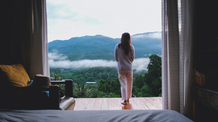 Wall Mural - Rear view of a woman standing on wooden balcony and looking at a beautiful mountains view on foggy day