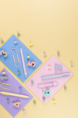 Wall Mural - Top view of pink, purple and blue notebooks on yellow background. Colorful pens, paperclips, numbers and pins. School, office wallpaper. Flat lay, copy space.