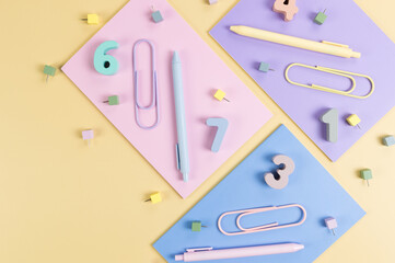 Wall Mural - Top view of pink, purple and blue notebooks on yellow background. Colorful pens, paperclips, numbers and pins. School, office wallpaper. Flat lay, copy space.