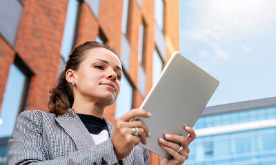 Wall Mural - Professional woman standing outdoors, using a digital tablet, with a modern building in the background