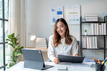 Wall Mural - young asian businesswoman smiling while working at her desk in office