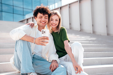 Wall Mural - Smiling beautiful woman and her handsome boyfriend. Couple in casual summer clothes. Happy cheerful family. Female and man having fun. They posing in the street. Hold phone, use mobile apps, outdoor