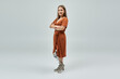 © Bliss - Confident young woman with prosthetic leg in brown dress, arms crossed, looking at camera
