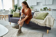 © Bliss - A woman sits on a couch in a living room, adjusting her prosthetic leg.