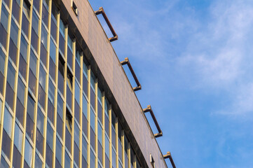 A tall building with a blue sky in the background. The building has a lot of windows and a balcony on the top