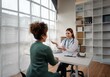 © YiuCheung - A female doctor sits across from a patient at a white table in a medical office.