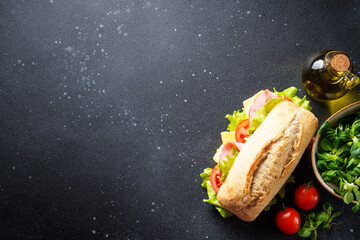 Canvas Print - Sandwich with lettuce, cheese, tomatoes and ham on black kitchen table with ingredients for cooking. Top view.