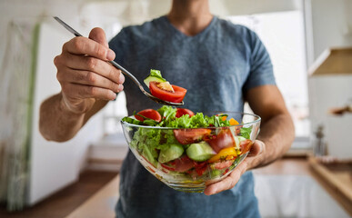 Young man eating a healthy vegan salad from a glass bowl in the kitchen. Vegan food concept