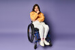 © Bliss - Trendy woman in casual attire sits in wheelchair against purple backdrop, hand on chin, gazing at camera