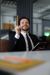 Sticker - A man in a suit is holding a pencil and smiling. He is sitting at a desk with a notebook and a ruler. Concept of creativity and productivity, as the man is likely working on a project or idea