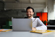 © Andrii Zastrozhnov - A man is sitting at a desk with a laptop open in front of him. He is smiling and he is enjoying his work