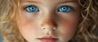 © GoDress - Close up portrait of a young girl with freckles and blue eyes looking directly at the camera.