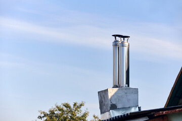 Two modern style chimneys from oven and fireplace stacked stainless steel on rural house roof covered with slate under clear blue sky with copyspace.