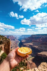 Hand holding a cookie against a stunning canyon landscape under blue sky.