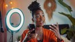 © ORG - photograph of phone and black woman talking on video podcast in the bedroom of her house. Happy and excited girl or influencer speaking on the internet or social media with a mobile and ring light