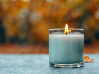 Wall Mural - Burning teal candle on empty table with autumn background