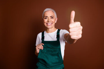 Sticker - Photo of optimistic charming attractive senior woman wear uniform thumb up isolated on brown color background