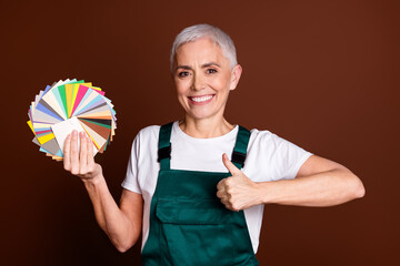 Wall Mural - Photo of optimistic lovely senior woman wear green uniform thumb up isolated on brown color background