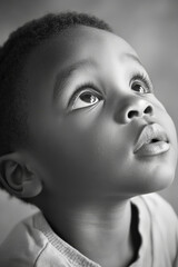 Sticker - Black and white portrait of a preschooler African American boy with short hair, expressive eyes, and clear skin, looking up in natural daylight.