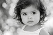 © wolfhound911 - Black and white portrait of a toddler Hispanic girl with neat hair and expressive eyes, standing playfully in natural daylight.