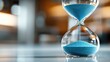 © svastix - A classic glass hourglass with brilliant blue sand slowly flowing from the top chamber to the bottom, representing the continuous passage of time with elegance and poise.
