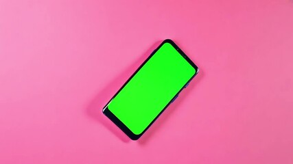 Top view of smartphone with a green screen on solid pink background