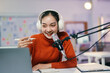 © Parichat - Young asian woman happily records a podcast in her modern home studio, speaking into a microphone and creating online content with technology