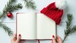 © яна винникова - Mock up. A red knit hat rests on an open blank notebook surrounded by pine branches and a red ornament, evoking a festive winter atmosphere