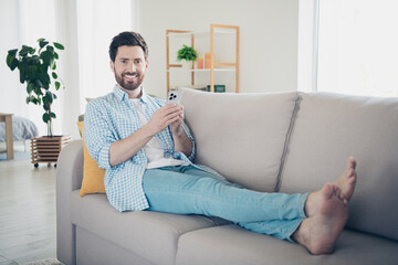 Sticker - Photo of handsome mature age adult man staying home in living room laying down couch barefoot comfortable and browsing news phone