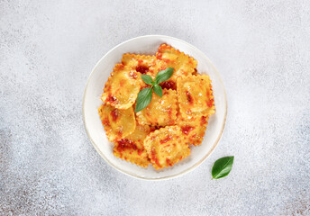 Ravioli with ricotta cheese, fresh tomato sauce and fresh basil on a gray background. Top view.