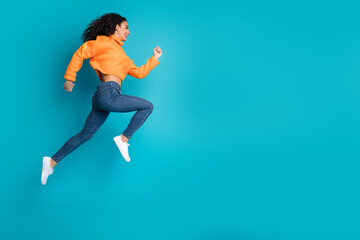 Wall Mural - Full length photo of charming positive girl wear orange sweater jumping high running empty space isolated blue color background