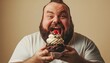 © Pattanan - Overweight man devouring a rich brownie cupcake on a solid cream colored background
