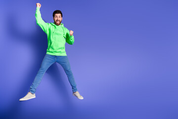 Poster - Full body photo of attractive young man jump raise fists winning dressed stylish green clothes isolated on violet color background