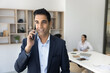 © fizkes - Young Indian male consultant distracted from group work in office make answer customers phone call. Business expert give professional advice to client discuss sales proposition schedule an appointment