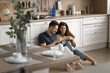 © fizkes - Cheerful positive young romantic couple sitting on heating floor in modern kitchen, toasting mugs with drink, having fun, laughing, enjoying leisure, break at new home