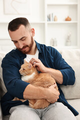 Wall Mural - Man petting cute ginger cat on sofa at home