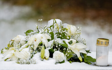 Flower arrangement. A beautiful white bouquet of flowers has been brought to the memorial site of the cemetery on a snowy winter day. Next to the flowers is a candle.