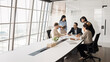 © fizkes - Multiethnic team of happy colleagues and Indian leader discussing business success at meeting table. Diverse employees talking to boss, smiling, laughing, enjoying successful teamwork. Wide shot
