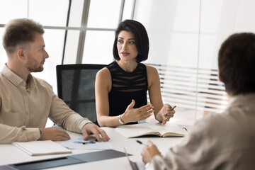 Poster - Beautiful young entrepreneur woman talking to male colleagues at office large table, explaining project strategy, speaking to coworkers. Board of directors, business partners meeting for negotiation