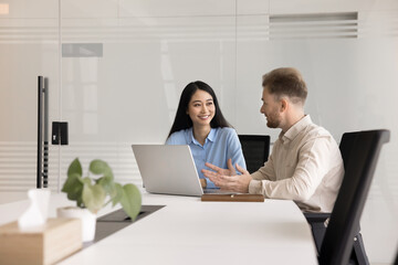 Poster - Couple of happy diverse business colleagues discussing online startup at laptop, talking, smiling. Project managers sitting at large table in office meeting room, using computer for teamwork,