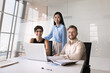 © fizkes - Multiethnic group of three positive professionals posing for portrait at workplace with laptop. Diverse business team meeting for teamwork at large office table, looking at camera, smiling
