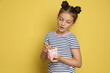 © New Africa - Pocket money. Cute girl putting coin into piggy bank on yellow background